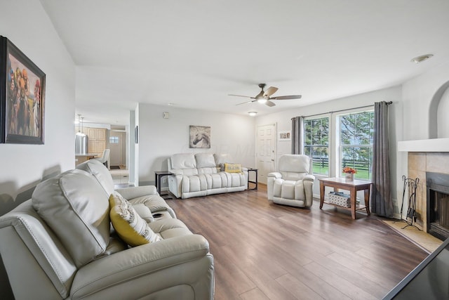 living room featuring a tile fireplace, wood-type flooring, and ceiling fan