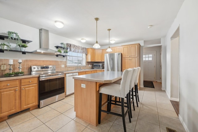 kitchen featuring pendant lighting, wall chimney range hood, sink, a kitchen island, and stainless steel appliances