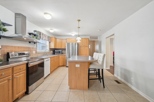 kitchen featuring a center island, a kitchen breakfast bar, wall chimney exhaust hood, decorative light fixtures, and stainless steel appliances