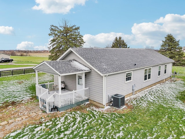 rear view of property with a deck with water view, central AC unit, and a lawn