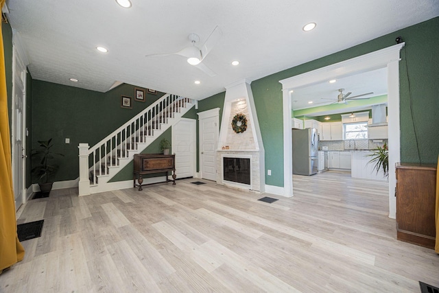 unfurnished living room with a fireplace, light hardwood / wood-style floors, ceiling fan, and sink