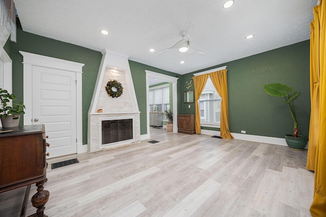 unfurnished living room featuring ceiling fan, a large fireplace, light wood-type flooring, and a textured ceiling