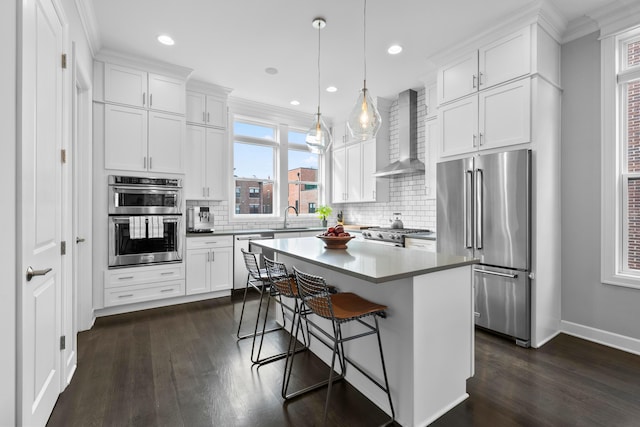 kitchen with wall chimney exhaust hood, hanging light fixtures, stainless steel appliances, a kitchen island, and white cabinets