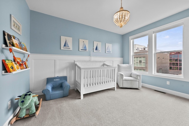 carpeted bedroom featuring a nursery area and a notable chandelier