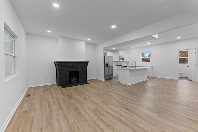 unfurnished living room with a brick fireplace, light hardwood / wood-style flooring, and sink