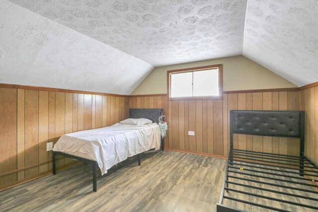 bedroom featuring lofted ceiling, a textured ceiling, wooden walls, and dark wood-type flooring