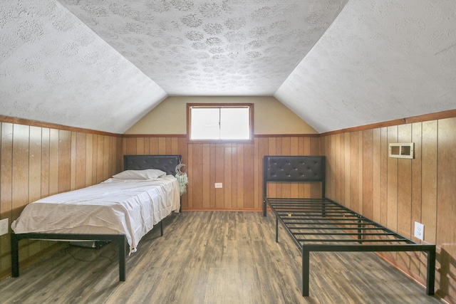 bedroom featuring wood walls, wood-type flooring, a textured ceiling, and vaulted ceiling