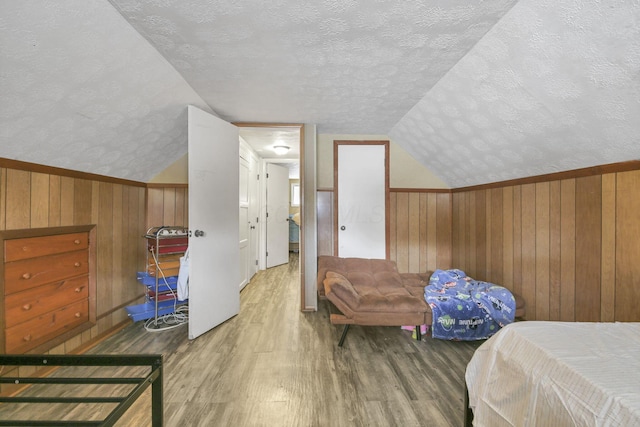 bedroom with lofted ceiling, wood-type flooring, a textured ceiling, and wooden walls