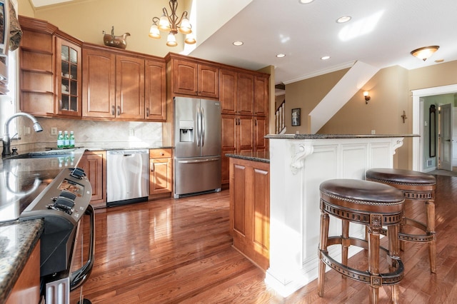 kitchen with sink, hardwood / wood-style floors, dark stone counters, decorative backsplash, and appliances with stainless steel finishes