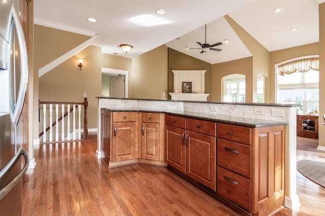 kitchen with a center island, stainless steel fridge, dark stone counters, wood-type flooring, and vaulted ceiling