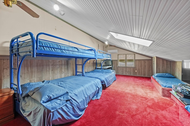 bedroom featuring carpet flooring, a wall mounted air conditioner, vaulted ceiling with skylight, ceiling fan, and wood walls