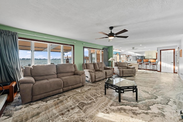 living room featuring a textured ceiling, a water view, and ceiling fan