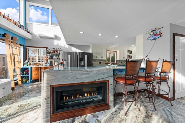 kitchen featuring tasteful backsplash, stainless steel fridge, white cabinetry, and stone countertops