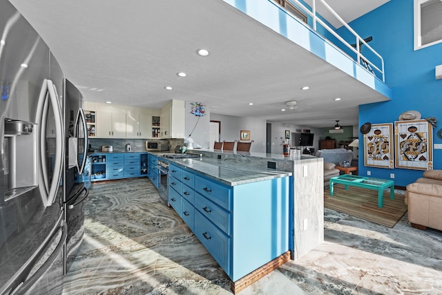 kitchen with backsplash, blue cabinetry, stone countertops, white cabinetry, and stainless steel appliances