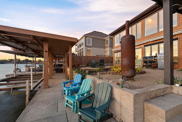 patio terrace at dusk with a boat dock, a water view, and grilling area