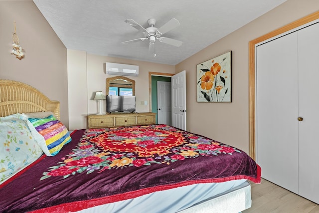 bedroom featuring ceiling fan, a wall mounted air conditioner, light hardwood / wood-style flooring, a textured ceiling, and a closet