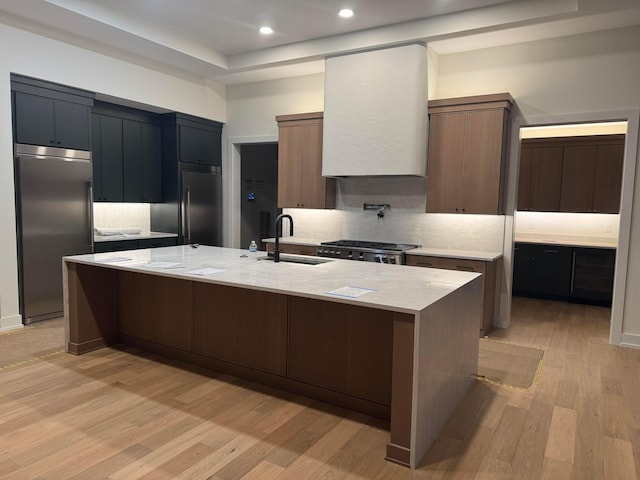 kitchen featuring built in refrigerator, light wood-type flooring, tasteful backsplash, and a sink