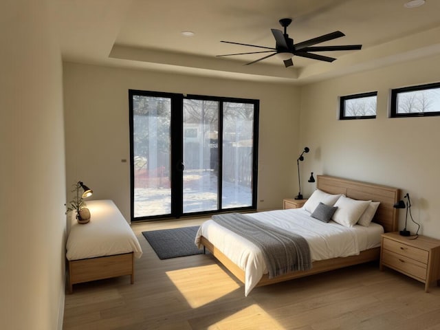 bedroom with light wood finished floors, a raised ceiling, and access to exterior