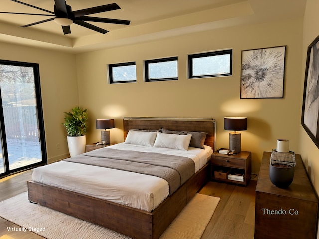 bedroom with access to exterior, ceiling fan, a raised ceiling, and wood finished floors