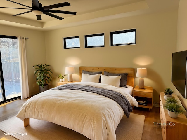 bedroom featuring ceiling fan, a tray ceiling, wood finished floors, and access to exterior