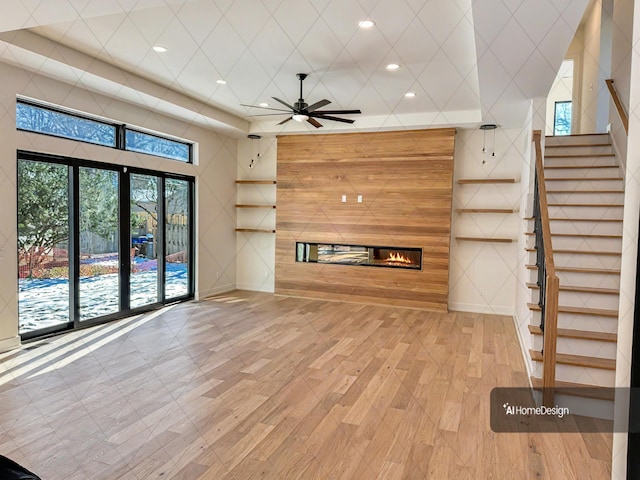 unfurnished living room featuring ceiling fan, recessed lighting, wood finished floors, stairs, and a glass covered fireplace