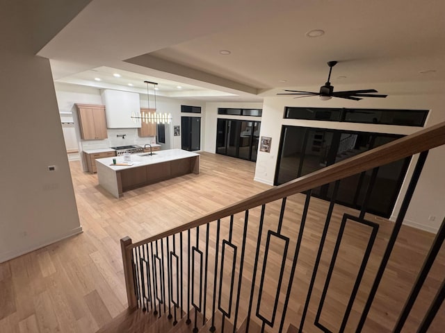 kitchen with ceiling fan, a kitchen island with sink, a tray ceiling, light countertops, and light wood-style floors