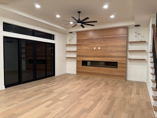 unfurnished living room featuring a glass covered fireplace, wood finished floors, recessed lighting, and stairs