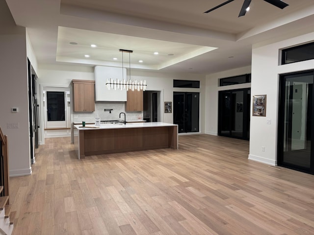 kitchen with light wood-style flooring, a tray ceiling, light countertops, and backsplash