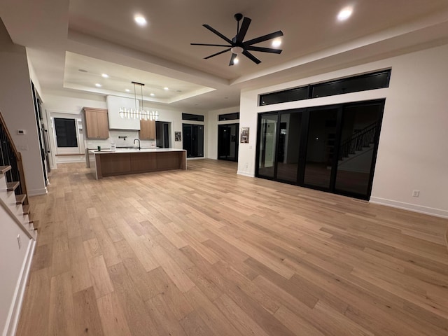 kitchen with baseboards, light wood-style flooring, open floor plan, a tray ceiling, and light countertops