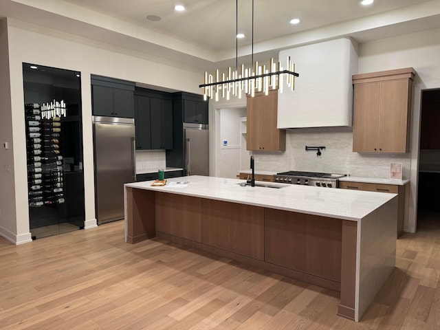 kitchen featuring appliances with stainless steel finishes, a large island with sink, a sink, and light wood finished floors