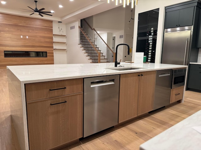 kitchen featuring light wood-style flooring, appliances with stainless steel finishes, open floor plan, a sink, and ceiling fan