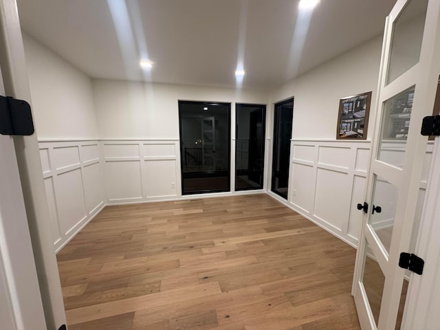 spare room featuring light wood-style floors, a decorative wall, and a wainscoted wall