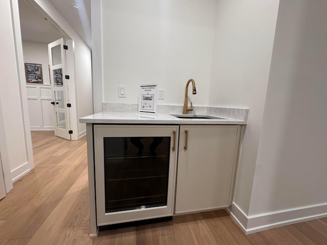 bar featuring beverage cooler, light wood-type flooring, a sink, and baseboards