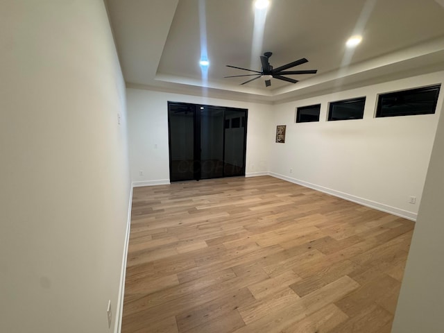 empty room with ceiling fan, light wood-type flooring, a raised ceiling, and baseboards