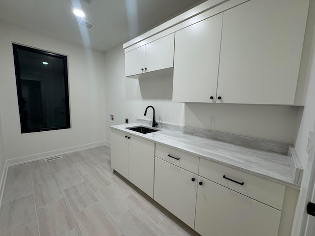 kitchen featuring light countertops, visible vents, white cabinets, a sink, and baseboards