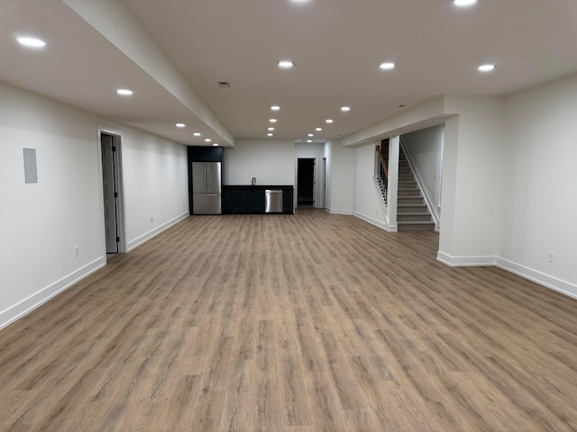 finished basement with light wood-style floors, freestanding refrigerator, stairway, and recessed lighting