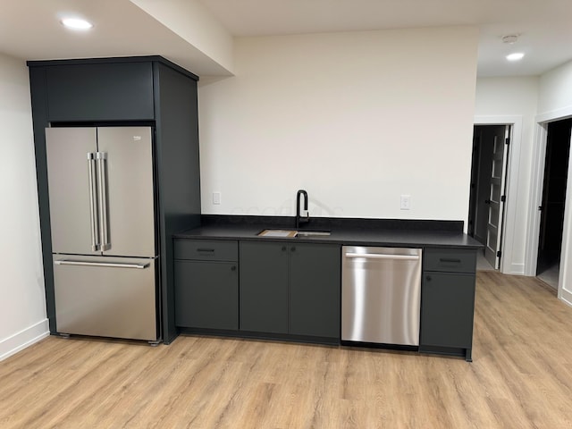 kitchen with light wood finished floors, appliances with stainless steel finishes, dark countertops, and a sink