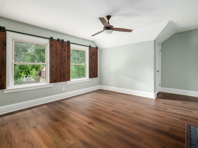 spare room with ceiling fan, a barn door, dark hardwood / wood-style flooring, and vaulted ceiling