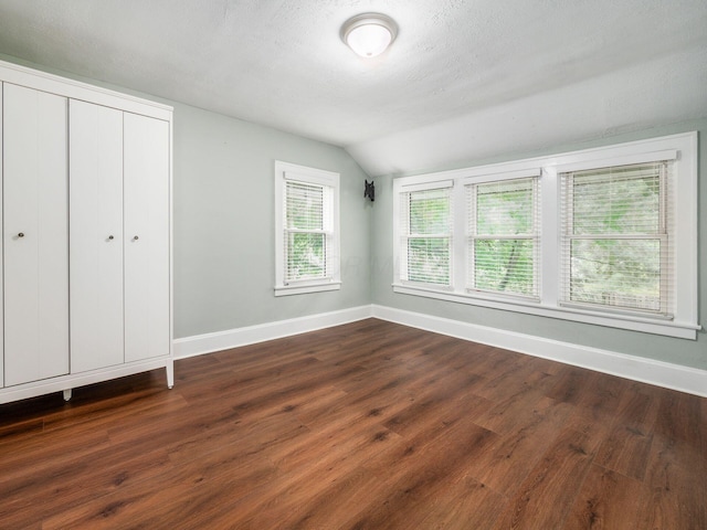 unfurnished bedroom with dark hardwood / wood-style floors, lofted ceiling, and multiple windows