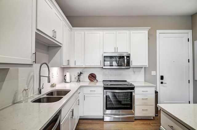 kitchen with white cabinets, sink, hardwood / wood-style flooring, tasteful backsplash, and stainless steel appliances