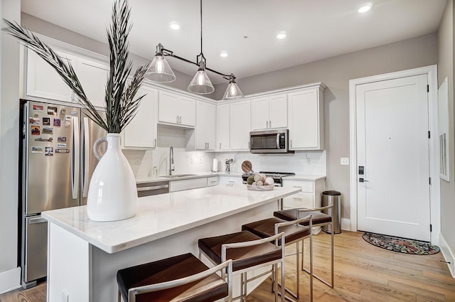 kitchen featuring light wood-type flooring, stainless steel appliances, sink, decorative light fixtures, and white cabinetry