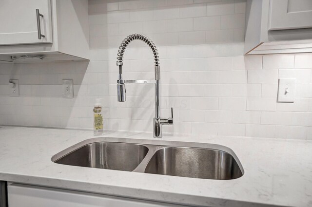 room details featuring light stone countertops, decorative backsplash, white cabinetry, and sink