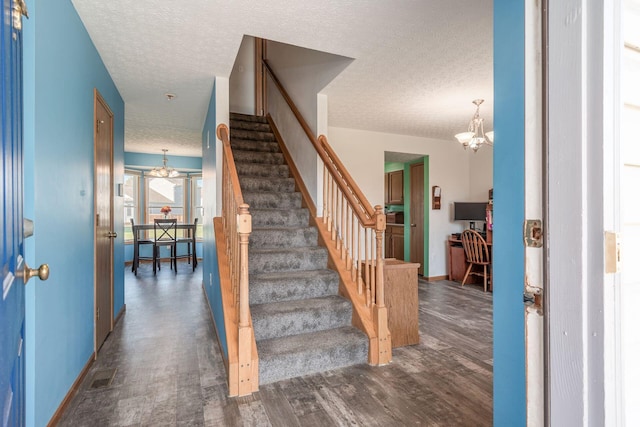 foyer entrance with a chandelier, dark wood-type flooring, and a textured ceiling