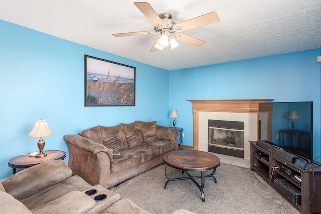 living room with a tiled fireplace, ceiling fan, light colored carpet, and a textured ceiling