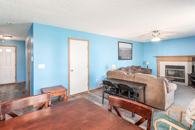 carpeted living room with a tiled fireplace, ceiling fan, and a textured ceiling