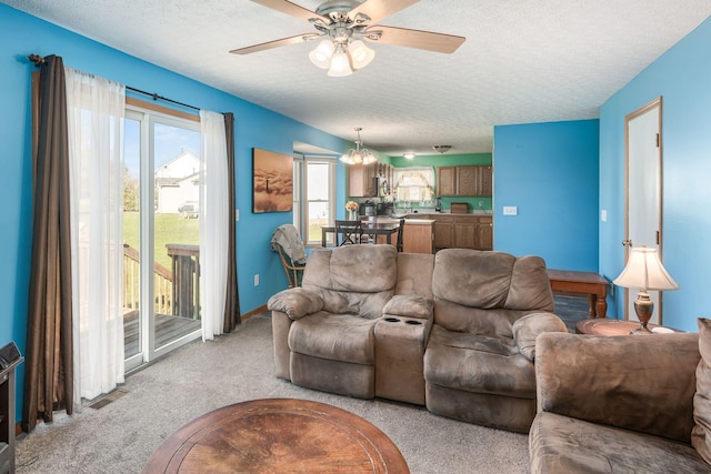 carpeted living room featuring plenty of natural light, ceiling fan with notable chandelier, and a textured ceiling