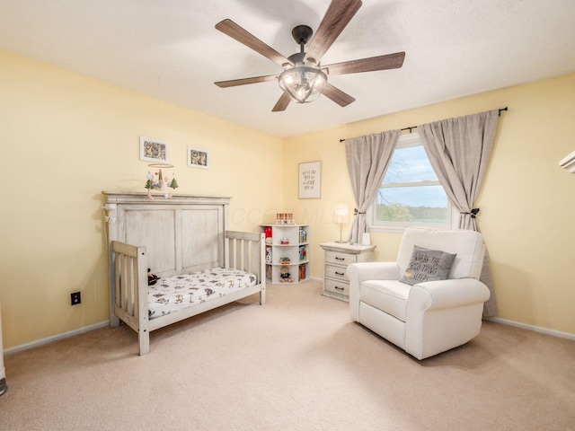 bedroom featuring a crib, light colored carpet, and ceiling fan