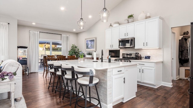 kitchen featuring appliances with stainless steel finishes, dark wood-type flooring, white cabinetry, hanging light fixtures, and an island with sink