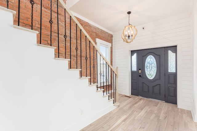 entryway with light wood-type flooring, ornamental molding, brick wall, and an inviting chandelier