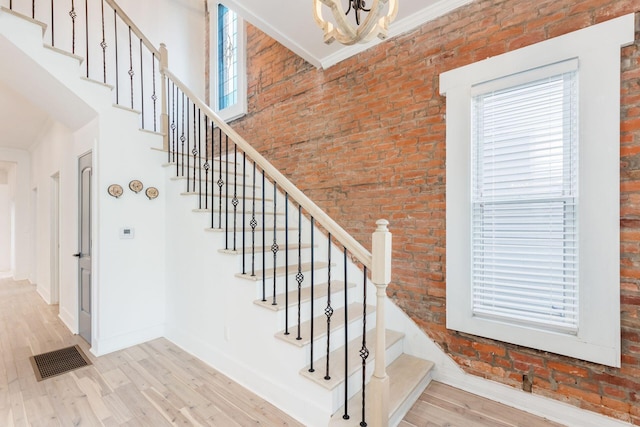 stairway with hardwood / wood-style floors, ornamental molding, and brick wall